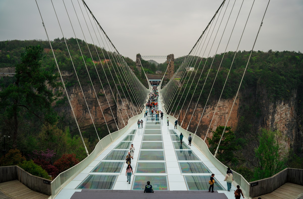Tourists walking across the transparent Zhangjiajie Glass Bridge suspended over Grand Canyon